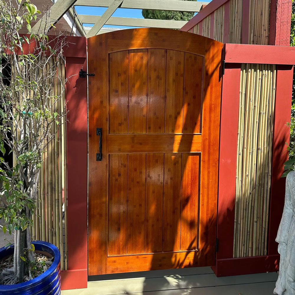 Amber-stained arched bamboo gate between red posts with a bamboo screen fence