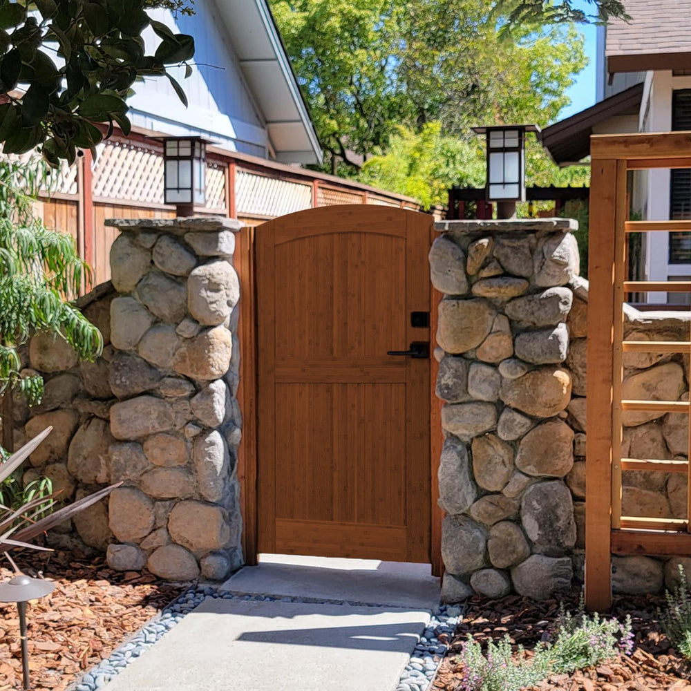 Natural-finish arched bamboo gate in a hedge arch with a lantern