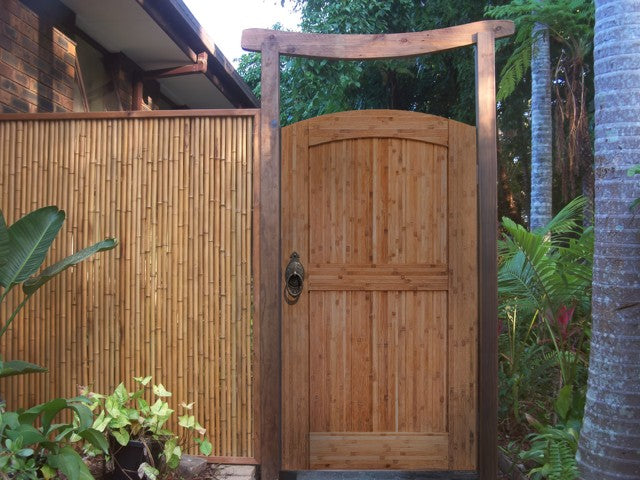 Natural-finish arched bamboo gate in a bamboo fence under a curved timber arch