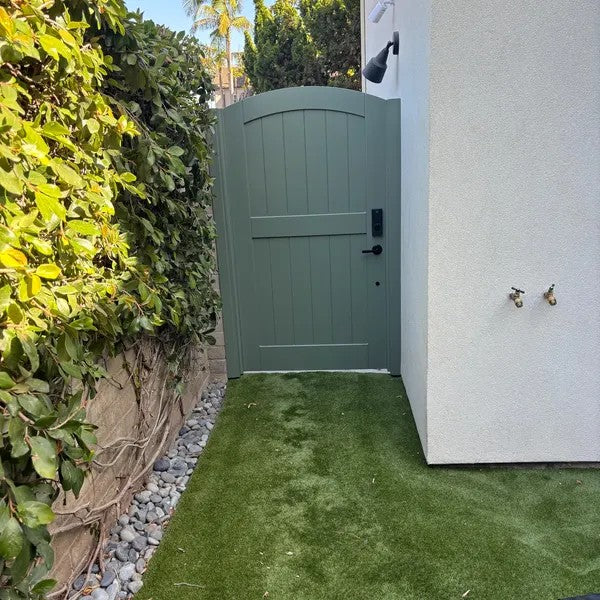 Sage-green painted arched bamboo gate with a keypad lock in a side yard